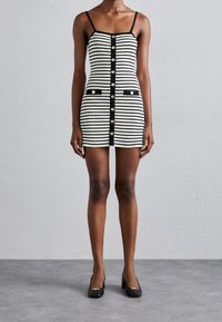 Robe rayée avec motif noir et blanc, présentant une coupe ajustée, une fermeture à boutons, deux poches avant et des bretelles fines.