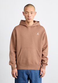 Sweatshirt à capuche marron en tissu doux. Comprend une poche avant et un petit logo Jumpman blanc sur la poitrine. Design à coupe ample.