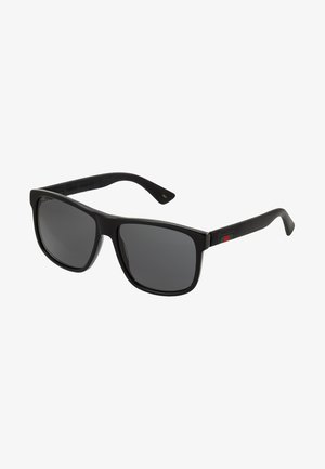 Ochelari de soare oversized negri cu lentile întunecate, ramă din plastic și dungi verzi-roșii-verzi pe brațe. Etichetă cu logo auriu pe lateral.