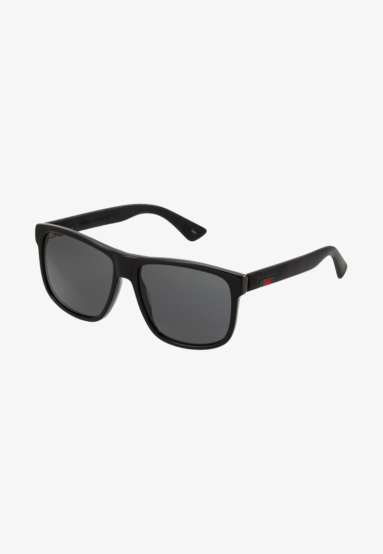Ochelari de soare oversized negri cu lentile întunecate, ramă din plastic și dungi verzi-roșii-verzi pe brațe. Etichetă cu logo auriu pe lateral.