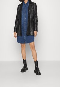 Svart läderblazer över en denim skjortklänning med knappframsida, spettsiga krage och knälånga svarta stövlar med tjocka sulor.