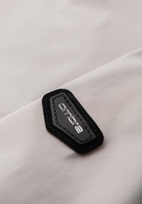 Gros plan d'une étiquette en tissu noire et grise avec un texte blanc cousue sur une surface textile lisse gris clair.