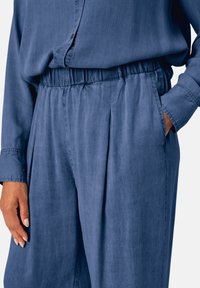 Pantalons en tissu tissé bleu avec des plis à l'avant, taille élastique et poches latérales, associés à une chemise assortie de couleur similaire.