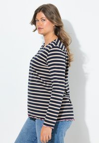 Top de rayas en azul marino y beige de manga larga con escote de barco y dobladillo en forma de ondas en color rosa, combinado con vaqueros azules. Textura de tela suave.