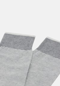 Calzini grigi caratterizzati da un polsino a coste, con un corpo grigio chiaro e accenti grigi scuri, realizzati in un tessuto a maglia testurizzato.