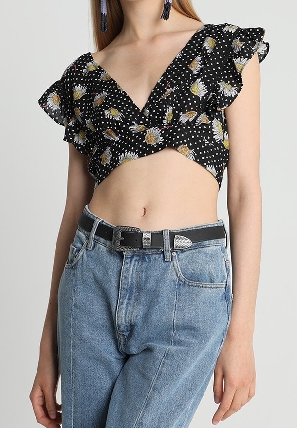 Top court noir avec imprimé marguerite et pois blancs, manches à volants, associé à un jean taille haute bleu clair et une ceinture noire.