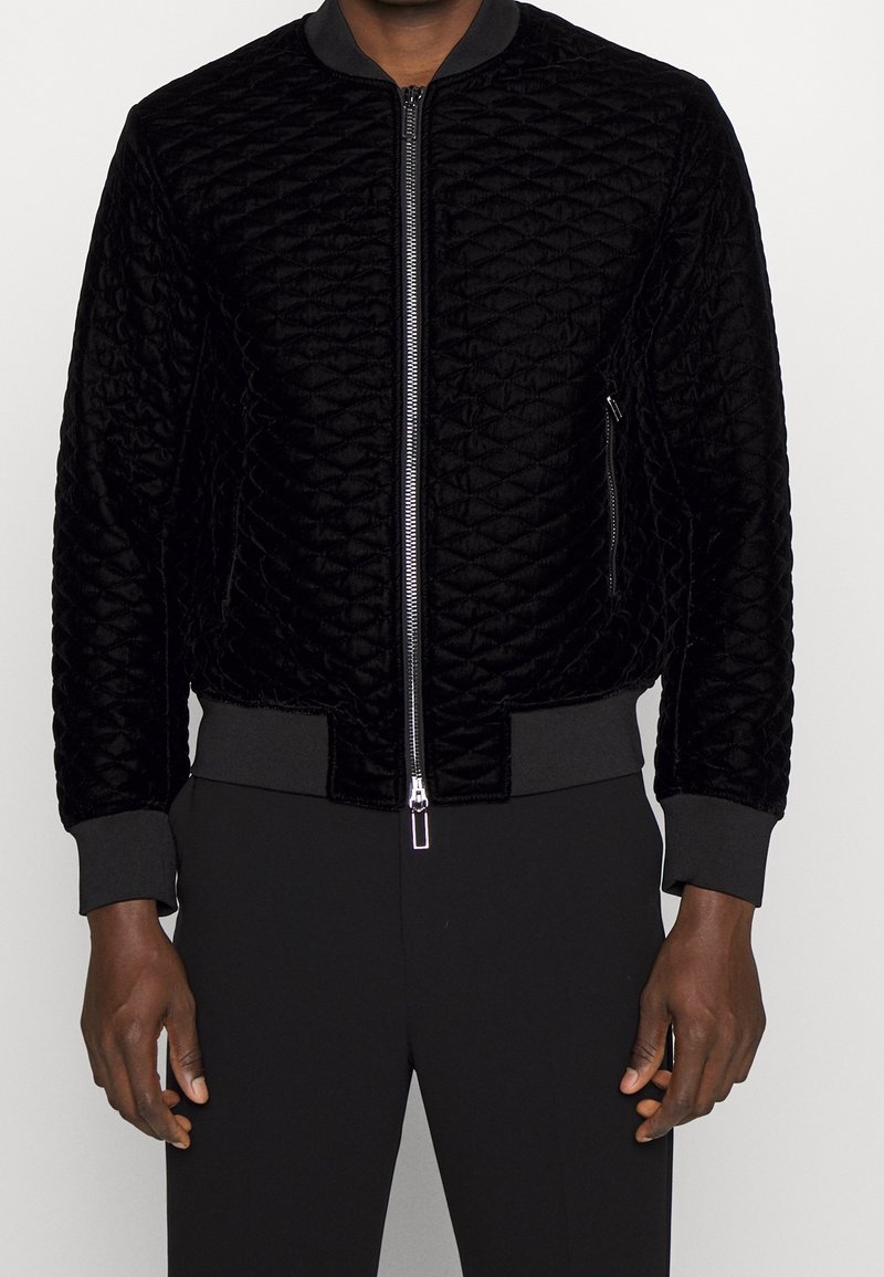 Svart kviltad bomberjacka i mjuk sammet med ribbade muddar och nederkant, med dragkedja fram och sidofickor.