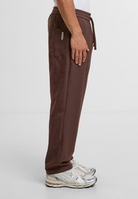 Bruine joggerpants met een slim fit, elastische tailleband, trekkoord en zijzak, gecombineerd met zilveren hardloopschoenen. Gemaakt van zacht materiaal.