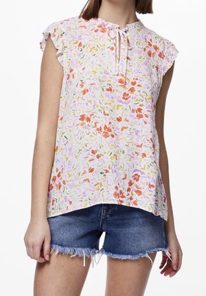 Blouse florale en tissu rose clair avec des manches à volants, détail de col en lien, présentant des motifs orange, violet et vert. Associée à un short en denim.