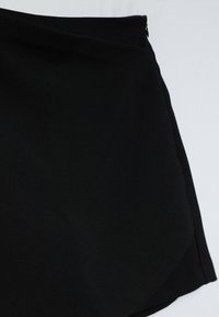 Close-up van een zwarte stoffen rok met een zijnaad en verborgen rits tegen een effen lichte achtergrond.