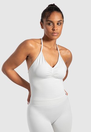 White halter top with a ruched front and adjustable straps, made of smooth fabric, paired with matching high-waisted leggings.