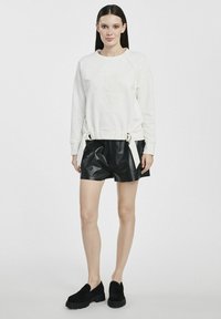 Biała bluza z wytłaczanym wzorem kwiatowym, ze ściągniętym w pasie, w połączeniu z czarnymi skórzanymi szortami. Czarne platformowe mokasyny dopełniają stylizację.