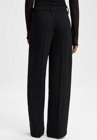 Zwarte wijde broek met een gladde textuur, elastische tailleband en riemlussen. Het detail van de achterzak versterkt het moderne ontwerp.