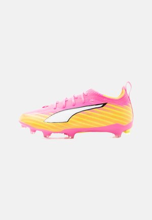 Felle roze en gele voetbalschoen met wit en zwart logo, gevormde noppen en trekkoord bij de hiel, zijaanzicht.