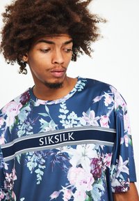 Blommig kortärmad t-shirt med en marinblå bas, vit "SIKSILK" logotyp och livliga rosa och gröna blommönster. Mjuk, slät tygkänsla.