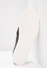 Chaussure Calvin Klein avec tige foncée, semelle blanche coussinée, semelle inférieure en caoutchouc texturée et détail du logo en relief sur le talon.