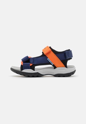 Sandale de sport avec semelle noire, lit de pied gris et brides réglables bleues et orange sur fond blanc.