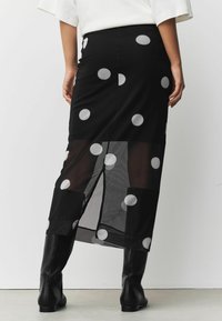 Must mustriga seelik, millel on läbipaistev materjal ja suured valged täpid, külgsuuna lõhe ning vormitud vöökoht, kombineeritud mustade põlvikute saapadega.