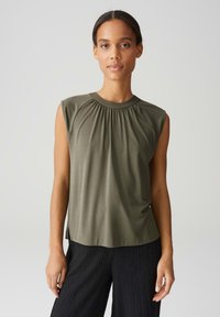 Olive green sleeveless top with a gathered neckline and a smooth texture, paired with black textured wide-leg pants.