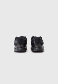 Chaussures de sport noires avec une tige en maille, des talons arrondis, des semelles en caoutchouc texturé et des accents perforés pour la respirabilité, vues de l'arrière.