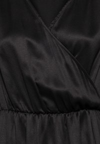 Svart satintyg med elastisk midja som är rynkad och en V-ringning med överlappande detalj, som visar en slät och något glansig textur.