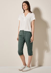 White short-sleeve blouse and green cropped pants with rolled cuffs. The outfit includes white sneakers with green accents and a relaxed fit.