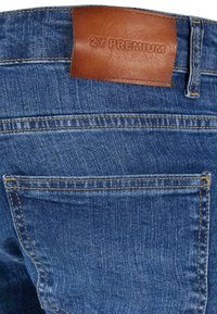 Poche arrière d'un jean en denim bleu avec coutures apparentes et patch en cuir marron embossé "2Y PREMIUM" à la taille.