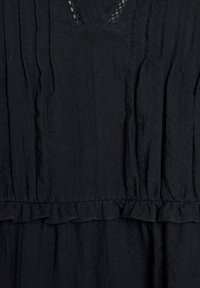 Schwarzes Kleid aus strukturiertem, zerknittertem Stoff. Verfügt über einen rüschierten Saum und einen V-Ausschnitt mit Spitzenverzierung. Schlichte, fließende Form. Keine Muster.