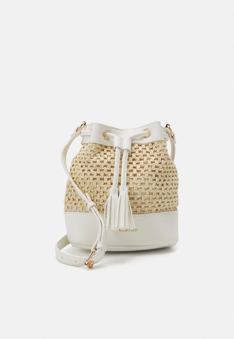 Woven bucket bag with a beige straw texture, white leather accents, tassel detail, and a shoulder strap. Gold hardware visible.
