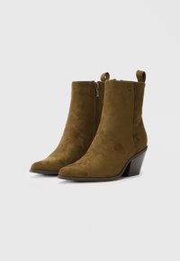 Botas de ante marrón hasta el tobillo con punta afilada y cremalleras laterales. Presentan costuras decorativas y un tacón bloque medio.