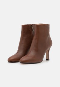Brune læderankelstøvler med spids tå og en slank hæl. Har en lynlås bagpå og glat tekstur. Simpelt, elegant design.