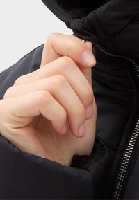 Czarna puchowa kurtka z wysokim kołnierzem; ręka zapina suwak z przodu; posiada srebrny zamek błyskawiczny i gładką, teksturowaną tkaninę.