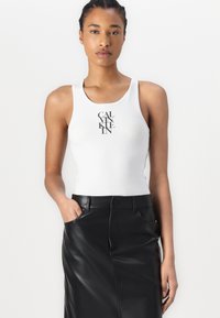 White tank top with a scoop neckline and black "CALVIN KLEIN" logo in the center, paired with a black leather skirt featuring side pockets.