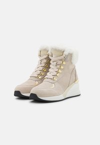 Bottines en suède beige avec doublure en fourrure, accents dorés et design perforé. Comprend des œillets métalliques et un talon compensé.