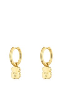 Ohrringe in Goldoptik mit polierter Oberfläche, mit einem hängenden, blumenförmigen Anhänger, auf dem "TOUS S925 LGG" eingraviert ist.