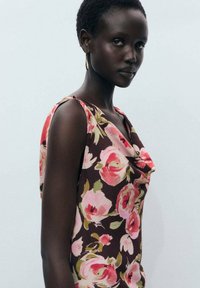 Top fără mâneci, floral, de culoare maron închis, cu modele de trandafiri roz și verzi, guler drapat, material moale și o ușoară strălucire.