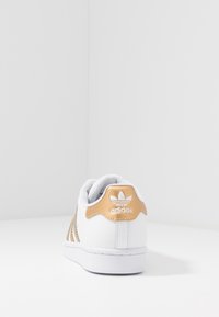 Biały sneaker ze złotymi akcentami, wykonany z teksturowanej skóry, z trzema perforowanymi paskami oraz wyściełanym kołnierzem przy pięcie z logo.