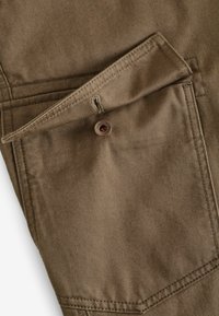 Khaki stoffen zak met een knoopsluiting, voorzien van een diagonale klep en contrasterende stiksels op een gladde, gestructureerde oppervlakte.
