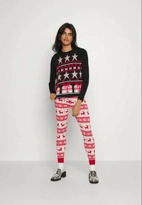 Maglione nero con motivo di stelle rosa e rosse, abbinato a leggings rossi con design di renne e fiocchi di neve bianchi. Scarpe argento.