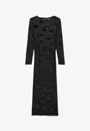 Robe longue noire en tissu doux avec un motif floral en relief légèrement texturé. Elle a des manches longues et un col rond.
