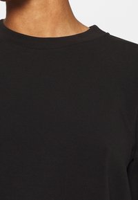 Black cotton t-shirt with a crew neck, featuring a smooth texture and a fitted design that highlights the neckline and shoulder seam.