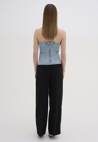 Top senza spalline in denim azzurro chiaro con taglio aderente, caratterizzato da una zip sul retro e dettagli di cucitura. Abbinato a pantaloni larghi neri.