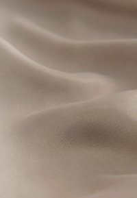 Beige kangas, joka on sileä ja pehmeä, virtaa kauniisti ja siinä on kevyt kiilto, mikä korostaa sen kevyttä ja joustavaa luonteenpiirrettä.