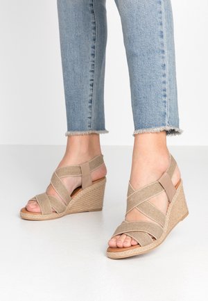 Beige kilehæle sandaler med krydsede stropper lavet af tekstureret stof og en glat detalje. Hæl indpakket i jute. Båret med cropped denim.