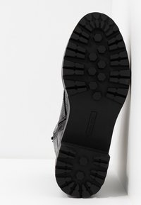 Zwarte leren laars met een gestructureerd bovenwerk, zijrits en een robuuste zwarte rubberen zool met een zeskantig profiel.