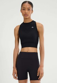 Czarny sportowy crop top z wysokim dekoltem i teksturowanym wzorem w zygzak. W połączeniu z czarnymi szortami o wysokim stanie z gładkiego, elastycznego materiału.