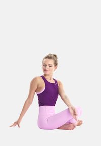 Naine lillaka tanki ja roosade retuusidega, istub jalad ristis ja teeb istuvat selgroo keerutamise jooga poosi, silmad kinni.