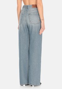 Jeans de tiro alto de pierna ancha en azul claro, confeccionados en denim, que cuentan con bolsillos traseros y un parche de cuero con la marca en la parte posterior de la cinturilla.