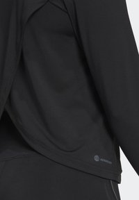 Svart träningsskjorta med mjukt, slätt tyg, en lös passform och en logotypaccents på sidan som heter "AEROREADY."