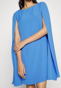 Short blue dress with a round neckline and cape sleeves. Made from lightweight fabric, features a smooth texture and loose fit.
